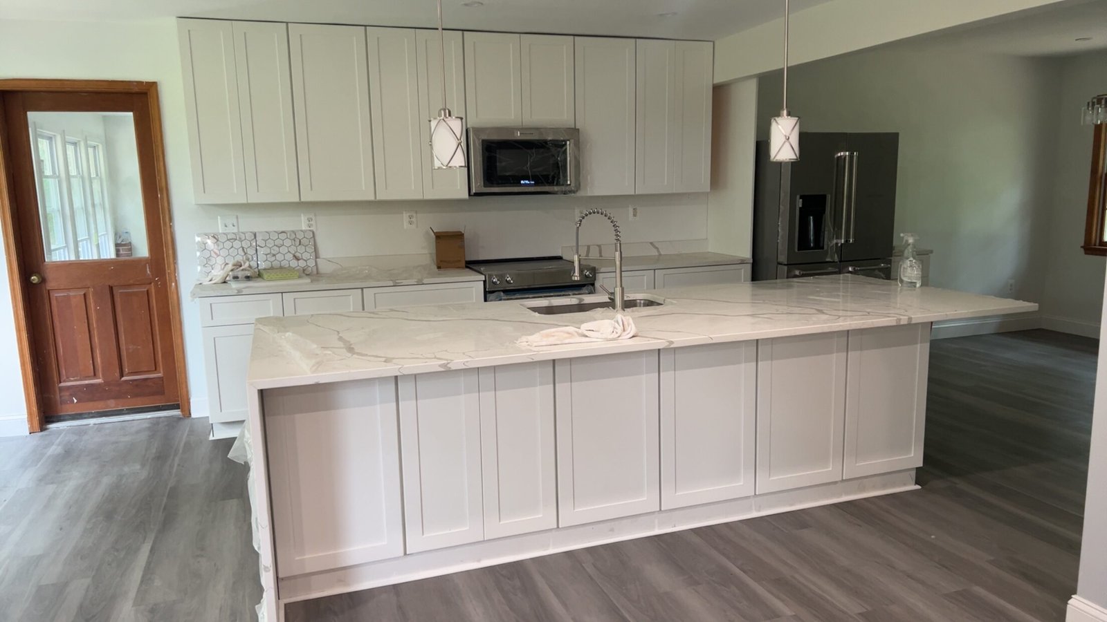 Kitchen with white cabinets, a large island, and gray laminate flooring.